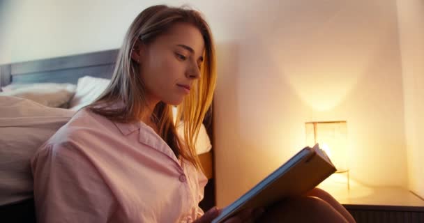 Ένα Ξανθό Κορίτσι Νυχτικό Κατά Καιρούς Διαβάζει Ένα Ενδιαφέρον Βιβλίο — Αρχείο Βίντεο