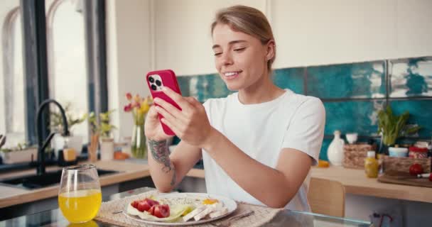 Blondynka Białej Koszulce Pracuje Czerwonym Telefonie Podczas Śniadania Słoneczny Poranek — Wideo stockowe