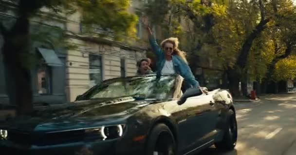一个戴太阳镜的金发女人和一个黑发女人坐在一辆灰色敞篷车里玩得很开心 旅途愉快 — 图库视频影像