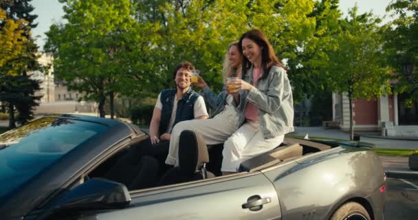 一群快乐的年轻朋友穿着牛仔夹克坐在出租车里喝着黄色的鸡尾酒 一个黑发女人和一个穿着白裤子的金发女人坐在敞篷车的高处 喝着黄色的鸡尾酒 — 图库视频影像