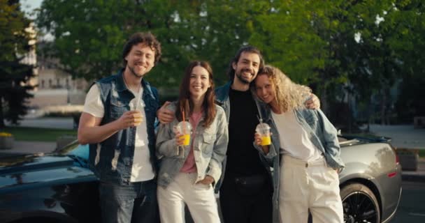 幸せな友人のグループが黄色のカクテルを手に車の近くに立っていて 幸せな夏の夜にカメラを見ています — ストック動画
