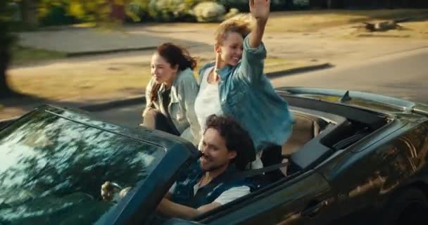一个快乐的三人组 一个男的和两个女的骑一辆灰色敞篷车 一个金发姑娘和一个黑发姑娘玩得很开心 挥挥手看相机 — 图库视频影像
