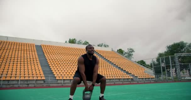 一名身穿黑色运动夏装的黑人男子在体育场用水壶进行训练 水壶上放着黄椅 — 图库视频影像