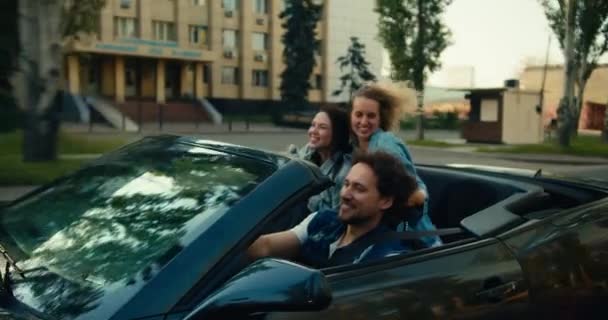 一个快乐的三人组 一个男的和两个女的骑一辆灰色敞篷车 一个金发碧眼的姑娘和一个黑发姑娘玩得开心快乐 坐出租车兜风愉快 — 图库视频影像