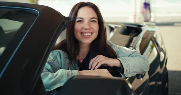 站在加油站的一辆深灰色出租车的前座上 一个漂亮的黑发姑娘摆姿势 — 图库视频影像