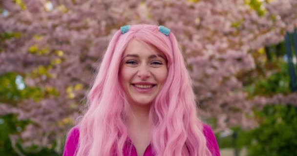 Крупный План Девушка Розовыми Волосами Позирует Перед Цветущим Розовыми Цветами — стоковое видео