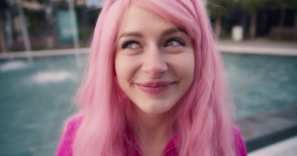 クローズアップ撮影 笑顔でカメラを覗き込むピンクの髪の少女の顔 明るい非公式な性格の概要 — ストック動画
