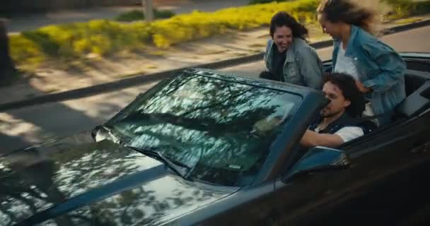 这对快乐的三人乘坐一辆灰色敞篷车 乘着微风 风吹着头发 年轻朋友们穿着牛仔夹克愉快地旅行 — 图库视频影像