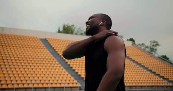 黒のスポーツウェアを着た黒人が競技場を歩き 体力訓練の後に関節を伸ばす — ストック動画