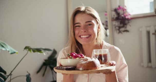 一个穿着白色睡衣的金发女孩手里拿着一份美味的早餐 尝着它的味道 咖啡果和面包 — 图库视频影像