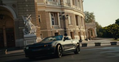 Koyu gri bir Cabriolet, muhteşem Rönesans mimarisi olan bir binanın önünden dönüyor..