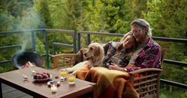 Bir kır evinde romantik bir akşam: sarışın bir adam ve sarışın bir kız battaniyeye sarılı bir kanepede oturuyorlar. Onların yanında açık renkli köpekleri oturuyor. Dağların manzarasıyla rahatla.