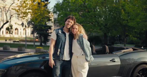 在阳光明媚的夏日 一对穿着牛仔夹克的可爱的情侣站在那里 面对着他们灰色出租车的背景 看着摄像机 — 图库视频影像