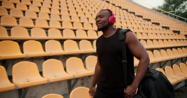 一名身穿黑色球衣 头戴红色无线耳机 身穿黑色皮衣 头戴黄色座椅的运动员在体育场中走来走去 寻找自己的位置 — 图库视频影像