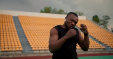 Siyah renkli, spor üniformalı bir sporcunun, tribünde sarı sandalyeler olan bir stadyumda boks yaparken yakın plan çekimi..