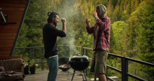 남자가 과산이 내려다 보이는 드넓은 발코니의 그릴에서 요리를 하면서 재미있는 — 비디오