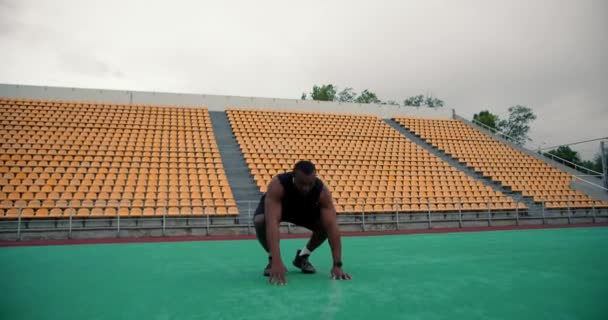一名身穿黑色运动服的黑人男子在一个有黄色看台的体育场里做了一个小便池运动 — 图库视频影像