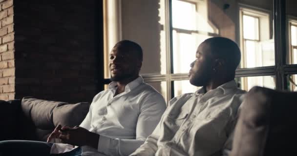 两个商人坐在一间阁楼式的阳光灿烂的办公室里聊天 身穿白衬衫的黑人工人坐在沙发上 提出了新的想法 — 图库视频影像