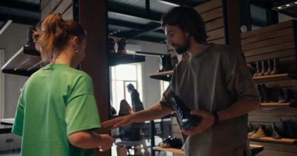 一位顾客 一位穿着棕色T恤的男士和一位穿着绿色T恤的鞋店女员工正在谈论选择鞋子的问题 — 图库视频影像