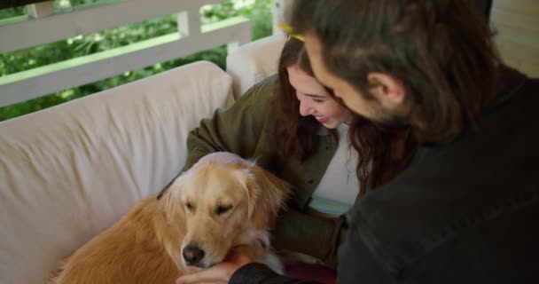 男人的黑发女孩在自然界中抚摸着一只浅色的狗 一个穿着绿色夹克的女孩和一条浅色的狗在自然界中的一个露台上互动 — 图库视频影像