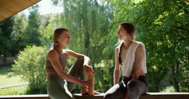 一个金发碧眼的女孩和一个棕色头发的女孩在一个美丽的绿色森林的背景下交谈 休闲和交流性质 — 图库视频影像