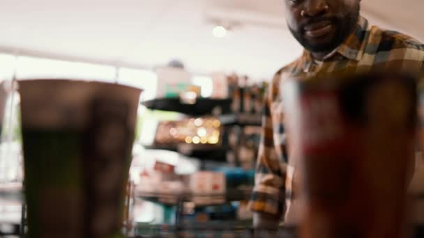 スーパーマーケットの床に2つのアイテムのうちの1つを選んだ黒人の男のクローズアップショット 店内の商品の選択 消費者は見る — ストック動画