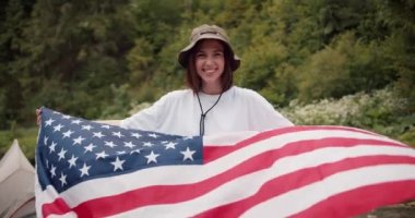 Beyaz tişörtlü esmer bir kızın portresi. Amerika Birleşik Devletleri bayrağıyla birlikte yeşil bir ormanın arka planında dalgalanan..