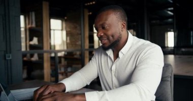 Black-skinned man in a white shirt rejoices at his office work success. An office worker works at a laptop and is very happy for his success.