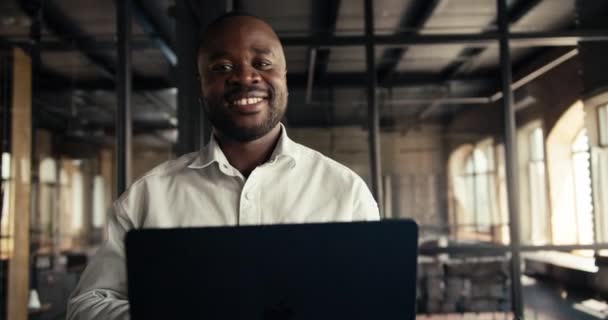 一位身穿白衬衫的年轻男性商人穿着黑色皮衣 头戴黑色笔记本电脑 在办公室里走来走去 看着摄像机 — 图库视频影像