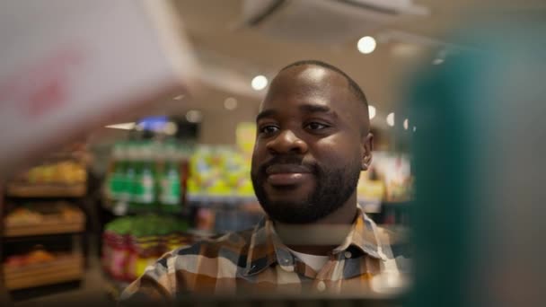 一名黑人男子在超级市场的地板上选择两种产品中的一种 — 图库视频影像