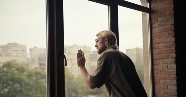 金发男人望着窗外下雨的地方 一个男人摘下眼镜 看着窗外的天气 — 图库视频影像