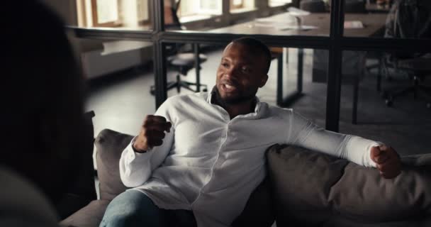 ソファに座っている白いシャツで彼の黒人の同僚とコミュニケーションするビジネスマンの最初の人物のビュー 2人のプロフェッショナルによるハッピービジネスコミュニケーション — ストック動画