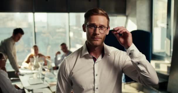 一个头戴眼镜 身穿白衬衫的金发男子站在办公室里 背对着他的高尔夫球腿 他在一个有着全景窗户的办公室的桌子旁工作 录像质量很高 — 图库视频影像