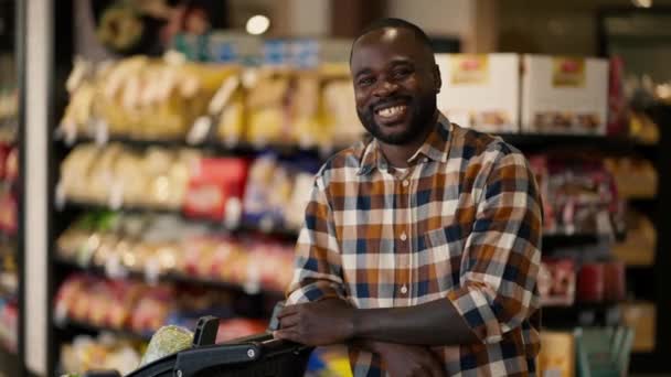 真っ黒な肌の色の男は スーパーマーケットのカートの近くに立って ポーズ カメラを見て笑顔 — ストック動画