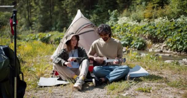 一个男的和一个女的游客坐在他们的帐篷边 男人弹吉他 女孩跳舞唱歌 — 图库视频影像