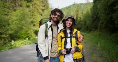 Bir adam ve bir kız turist dağ ormanının arka planında kamerayla yürüyüş yapmak için özel kıyafetler giyiyorlar..