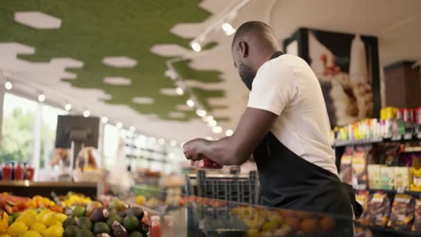 黒い肌の色の男がスーパーマーケットのカウンターから期限切れの製品を拾う 製品品質管理について — ストック動画