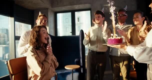 同事们给了一个穿着棕色衬衫的女商人一个惊喜 并给她带了一个蛋糕和蜡烛 这个女孩对这个惊喜很满意 并且在办公室里拥抱了她的朋友 — 图库视频影像