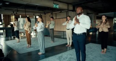 Ofisteki ekip meditasyon ve yoga ile meşgul. Ofis çalışanları halıya çıkıp ellerini önlerinde kavuşturuyorlar..
