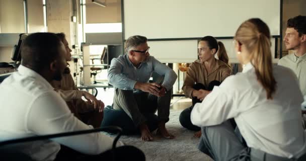 ビジネスススーツのグループセラピーの人々は オフィスでマットの上に座っている間 自分自身の間でコミュニケーションをとります — ストック動画