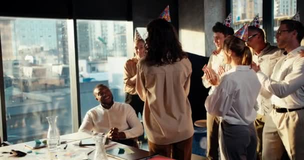 祝贺在办公室工作的一个商业团队中的黑人男性商人 戴着节日礼帽的同事们给一个男人带来了一个带有蜡烛的蛋糕 — 图库视频影像