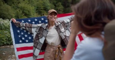 Bir kızın, Amerika Birleşik Devletleri bayrağıyla yeşil bir ormanın arka planında duran arkadaşının fotoğrafını çekmesinin ilk yolu..