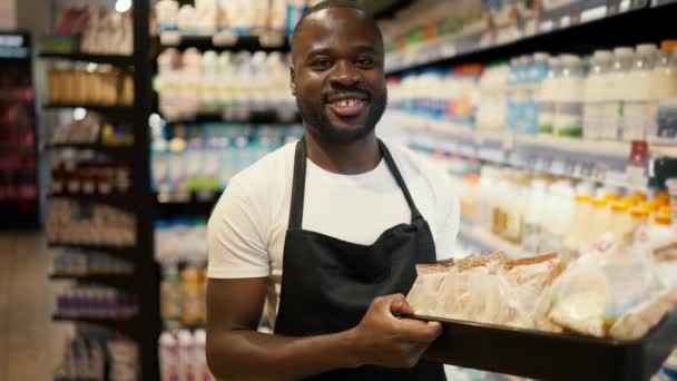 一个身穿白色T恤的黑皮肤男子和拿着一盒奶酪的黑围裙的画像 在奶牛场摆出一副笑脸 — 图库视频影像