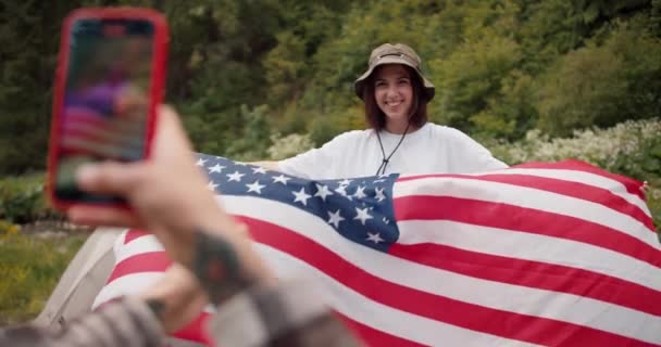 女の子を近づける撮影は 彼女のガールフレンド 彼女の手にはアメリカの旗を持つブルネットの少女の写真を撮ります それから彼女は彼女が反対した写真を見せます — ストック動画