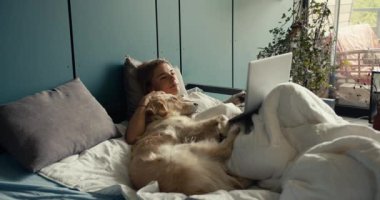 Sarışın bir kız köpeğiyle yatağa uzanıyor ve sabahları dizüstü bilgisayarında film izliyor. Hayvanlarla tatiller.