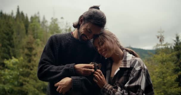 青いセーターの男とブロンドの女の子が ブルネットの男に抱かれている猫を脳卒中させている 山の森を見下ろす田舎の家でペットと一緒に休む — ストック動画