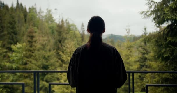 緑色のジャケットの幸せなブルネットの少女は 山の緑豊かな森を見下ろすカントリーハウスのバルコニーに行く — ストック動画