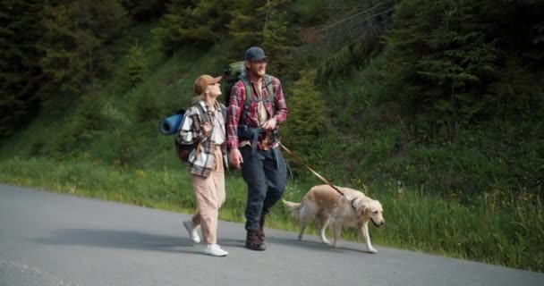 赤いシャツのブロンドの男とブロンドの女の子は 彼らは新しい領土を旅する森に沿って彼らの犬のライトカラーで歩くための特別な服で — ストック動画