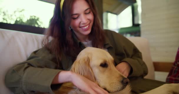 特写镜头 一个黑发女孩 头戴黄色绷带 身穿绿色夹克 在大自然中抚摸着一条浅色的狗 — 图库视频影像