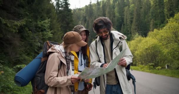 観光客のトリオは迷子になり 次の行き先を把握するための地図を見ています ハイキング服の人々は 山岳地帯の隣にどこを持っているかを整理します — ストック動画